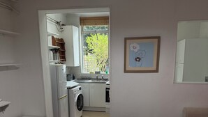Een knus woongedeelte met een kitchenette, een wasmachine, een eettafel en een rode bank.