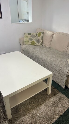 Ein Zimmer mit einem weißen Tisch, einem beigefarbenen Sofa mit gemusterten Kissen und einem Spiegel an der Wand.
