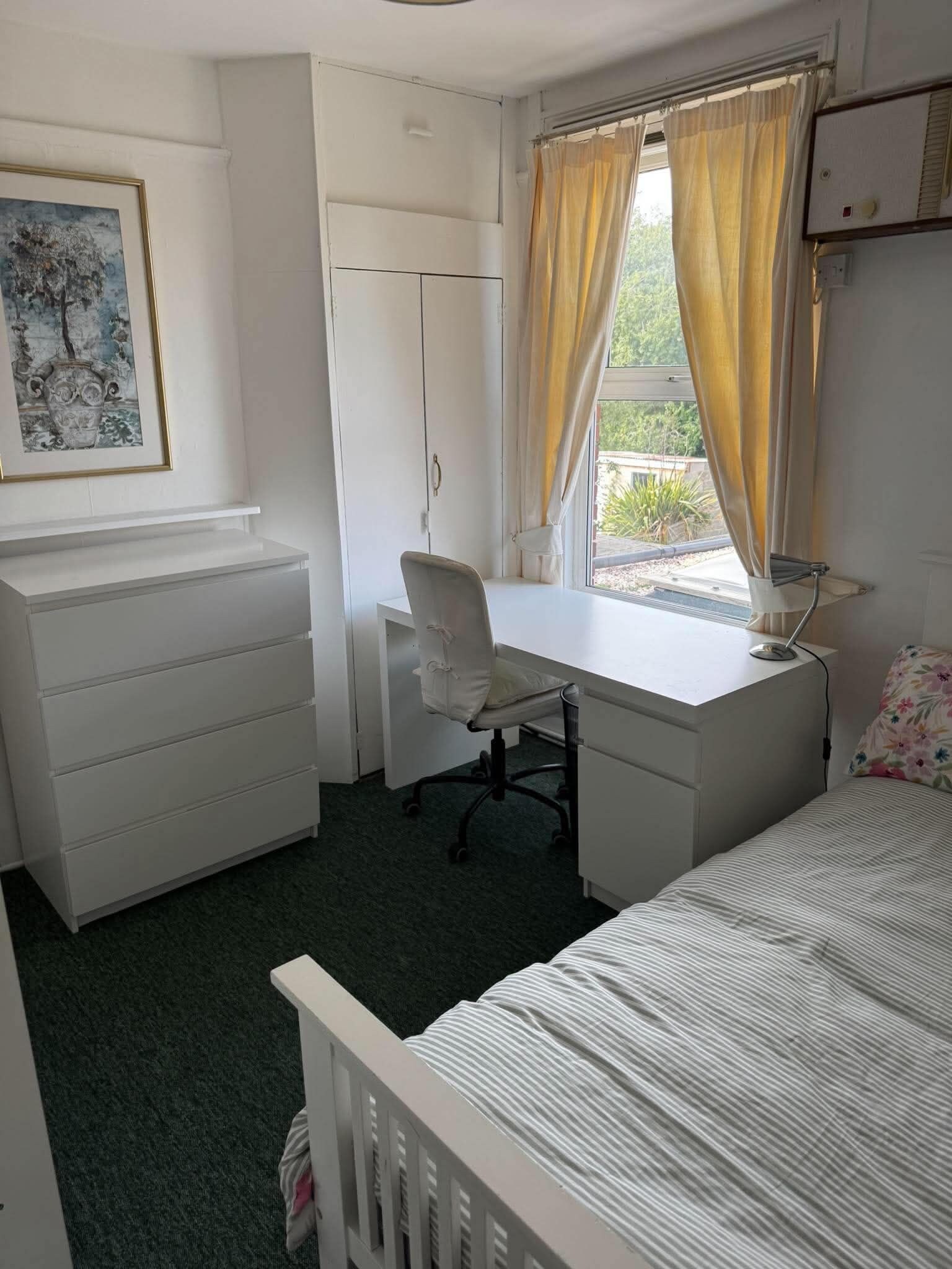 Ett sovrum med en säng, ett skrivbord, en stol, en garderob och ett fönster med gardiner.