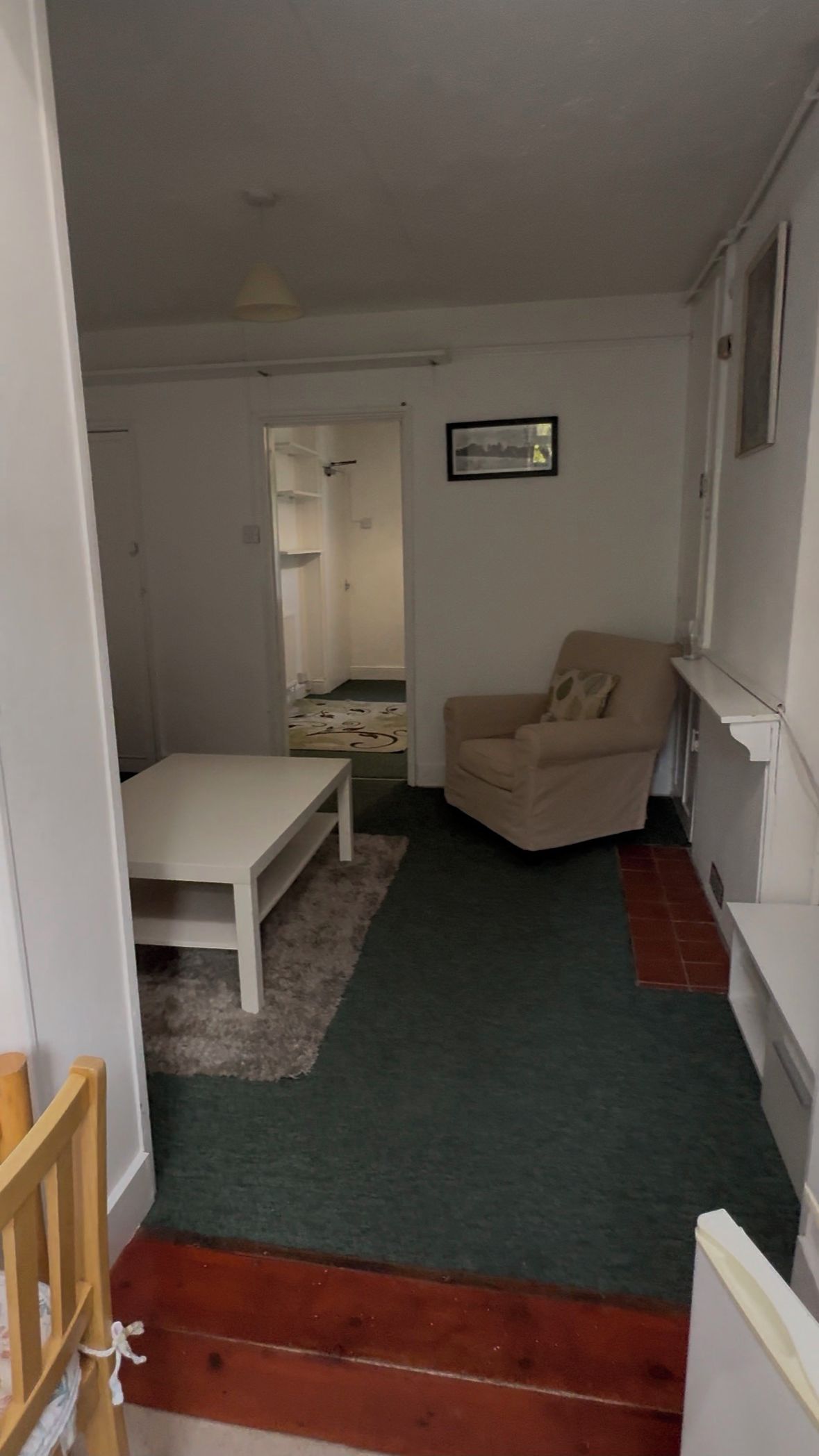 Une petite pièce au mobilier minimaliste, avec un seul fauteuil beige, une table blanche et un tapis vert.
