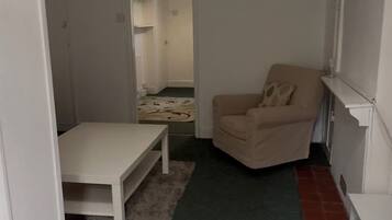 Une petite pièce au mobilier minimaliste, avec un seul fauteuil beige, une table blanche et un tapis vert.