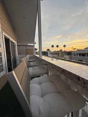A covered outdoor seating area with a view of the sunset and palm trees. - Home Away By the Beach 2! Beautiful 3-bedroom Newport Beach Upstairs Condo (Newport Beach)