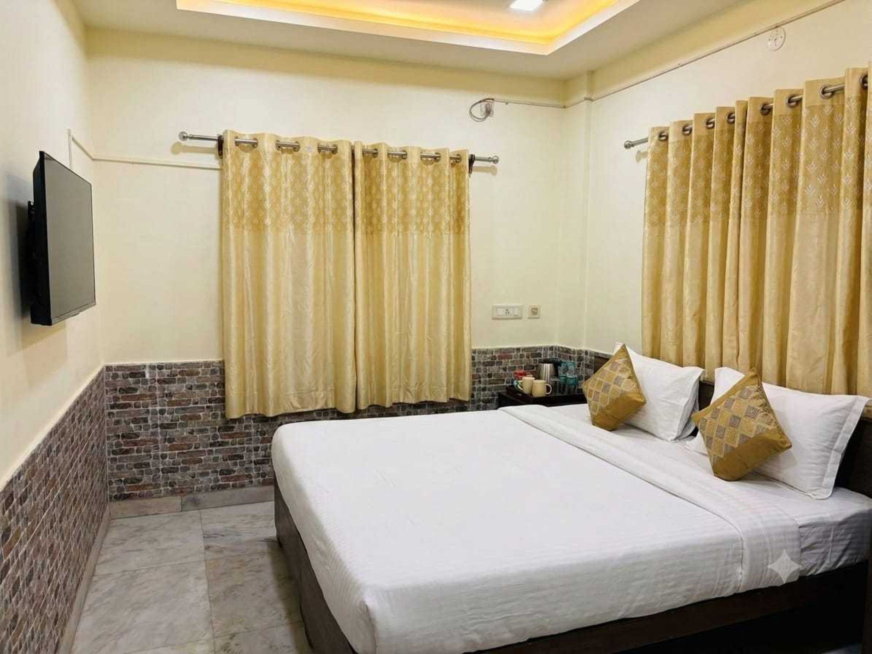 A hotel room with a bed, curtains, a flat-screen TV, and a brick accent wall.