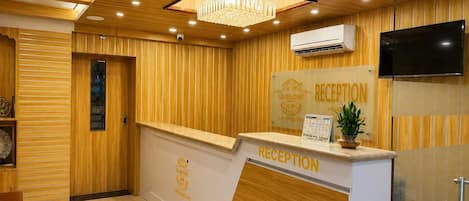 Un'area di accoglienza con parete rivestita in legno, scrivania della reception, lampadario e televisore a parete.