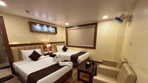 Quarto de hotel com duas camas, um sofá, uma mesinha e um ventilador de teto.