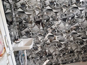 Casa de banho com lavatório e parede revestida de azulejos geométricos e refletivos.