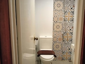 Un baño con inodoro, cortina de ducha con estampado floral y una toalla sobre el asiento del inodoro.