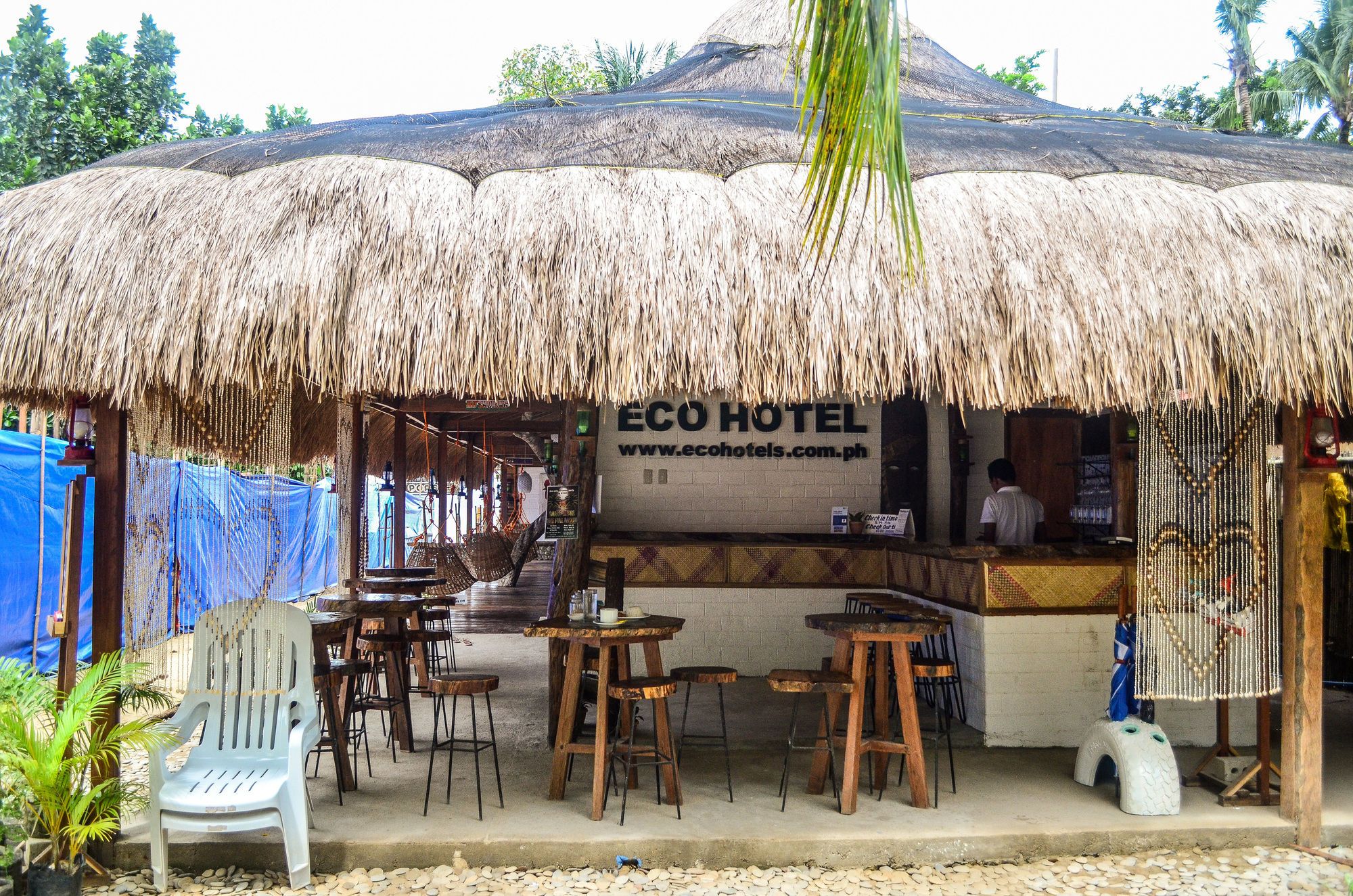 Ein Außenbereich mit Strohdach, Holztischen und -stühlen sowie einem Schild für ECO HOTEL.