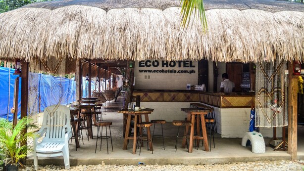 Area esterna con posti a sedere, un tetto di paglia, tavoli e sedie in legno e un cartello che indica ECO HOTEL.