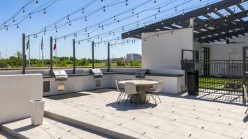 Un patio al aire libre con una parrilla, asientos e iluminación colgante.