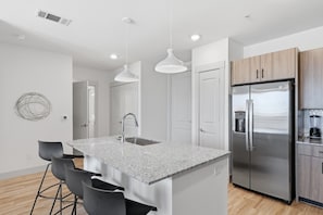 A modern kitchen with a central island, stainless steel appliances, and pendant lighting. - Stylish 2B near Legacy West Wi-Fi, Fitness, Pool (Frisco)