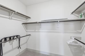 Ein begehbarer Kleiderschrank mit Metallregalen, einer Kleiderstange und einem kleinen Bügelbrett.