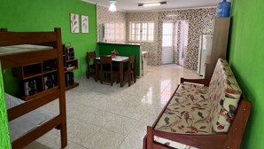 Una habitación con una cama litera, una mesa de comedor con sillas, un sofá, una zona de cocina con refrigerador y dispensador de agua.