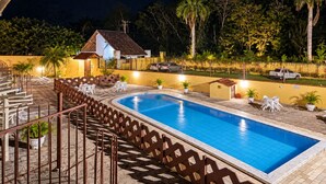 Una piscina con muelle de madera y sillas, rodeada por una valla y árboles.