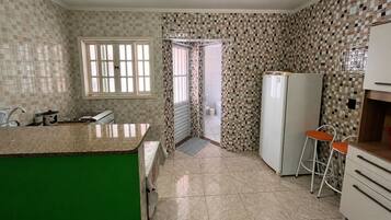 Eine Küche mit gefliestem Rückspritzschutz, einem Fenster, einem Kühlschrank und einem Barhocker.