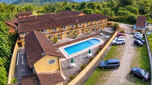 Un hotel con piscina, varios automóviles estacionados y montañas al fondo.