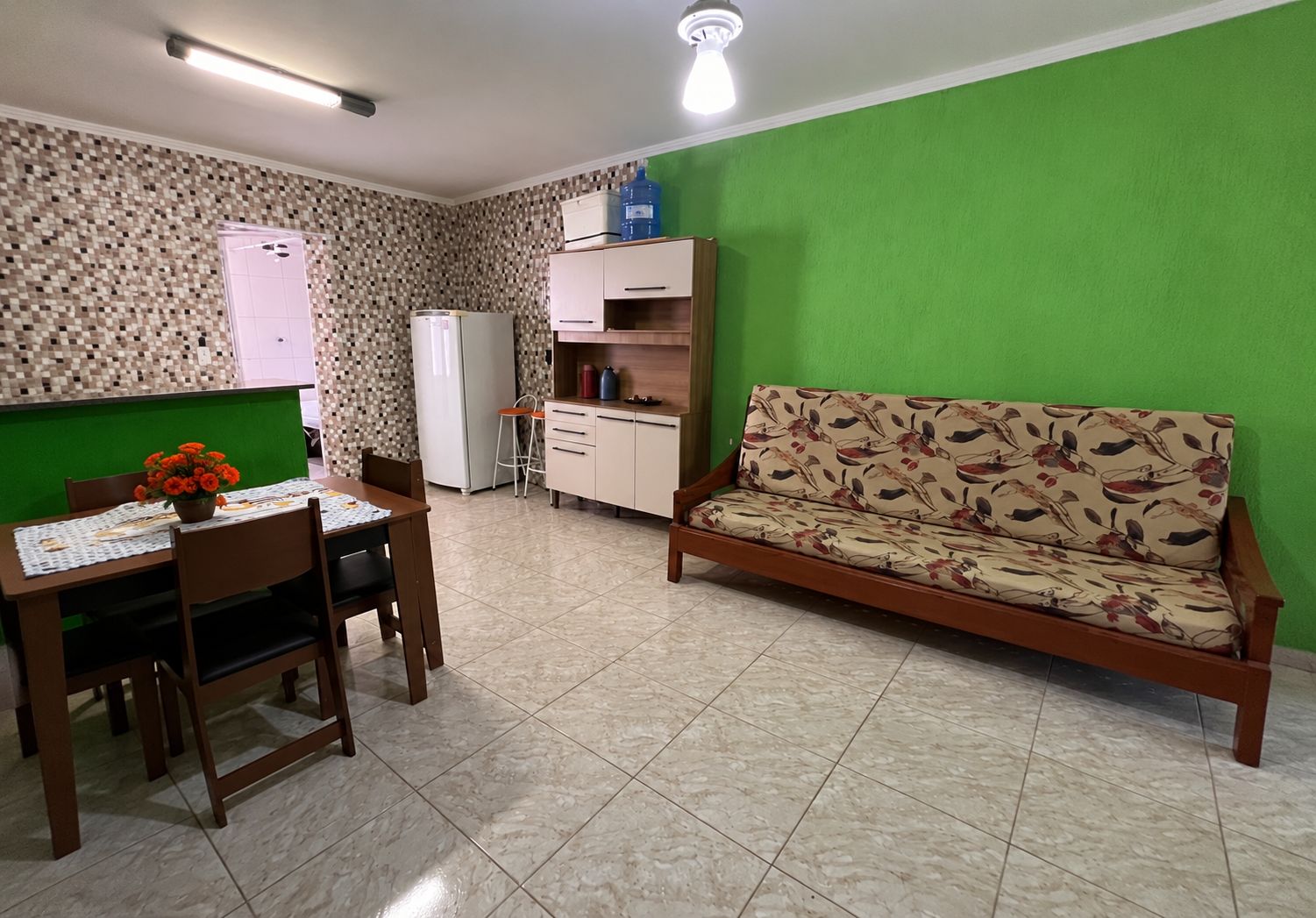 Ein Wohnzimmer mit einer Couch, einem Esstisch mit Stühlen, einem Kühlschrank und einem Wasserspender.