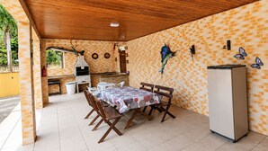 Un patio al aire libre con pared de ladrillo, techo de madera, suelo de baldosas, una mesa con sillas, un refrigerador y una parrilla.
