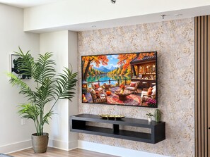 A living room with a mounted TV, a wooden floor, and a large potted plant. - Awe Walk to Amazon HQ, Wholefoods•King bed Met Park Gym Mins to Metro/DC/Mall (Arlington)