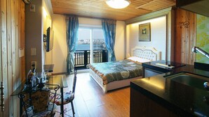 Ein Schlafzimmer mit einem Bett, einem Fenster mit Vorhängen, Blick auf eine Stadtlandschaft, einem kleinen Tisch mit einem Glas und einem Stuhl.