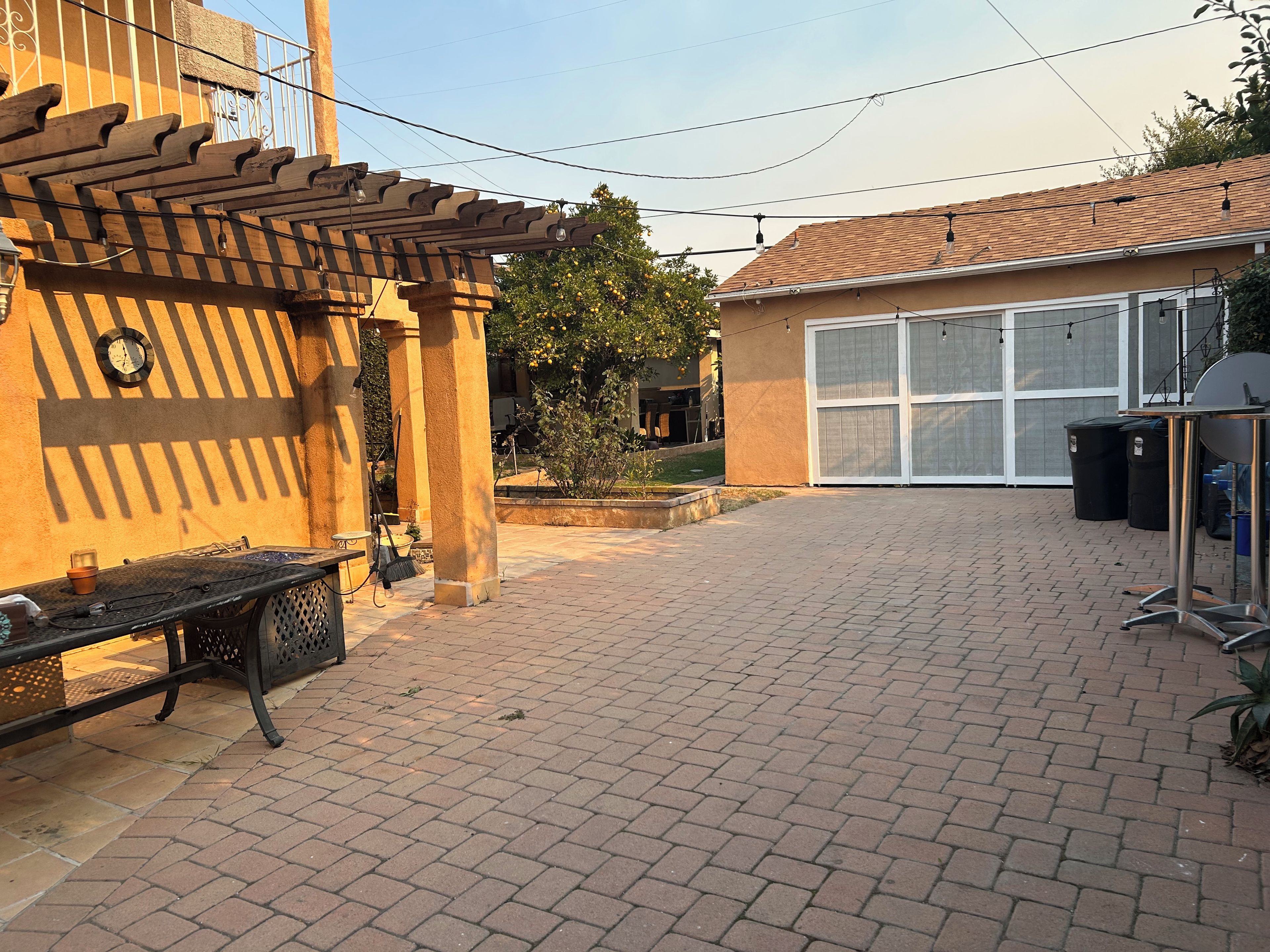 A paved patio area with a pergola, a garage, and a trash bin.
