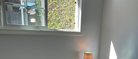 A white desk with a lamp, a black office chair, and a window with a view of greenery.