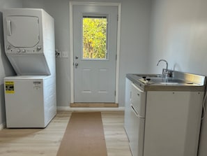 Ett tvättrum med tvättmaskin och torktumlare, ett handfat och en dörr med utsikt över träd.
