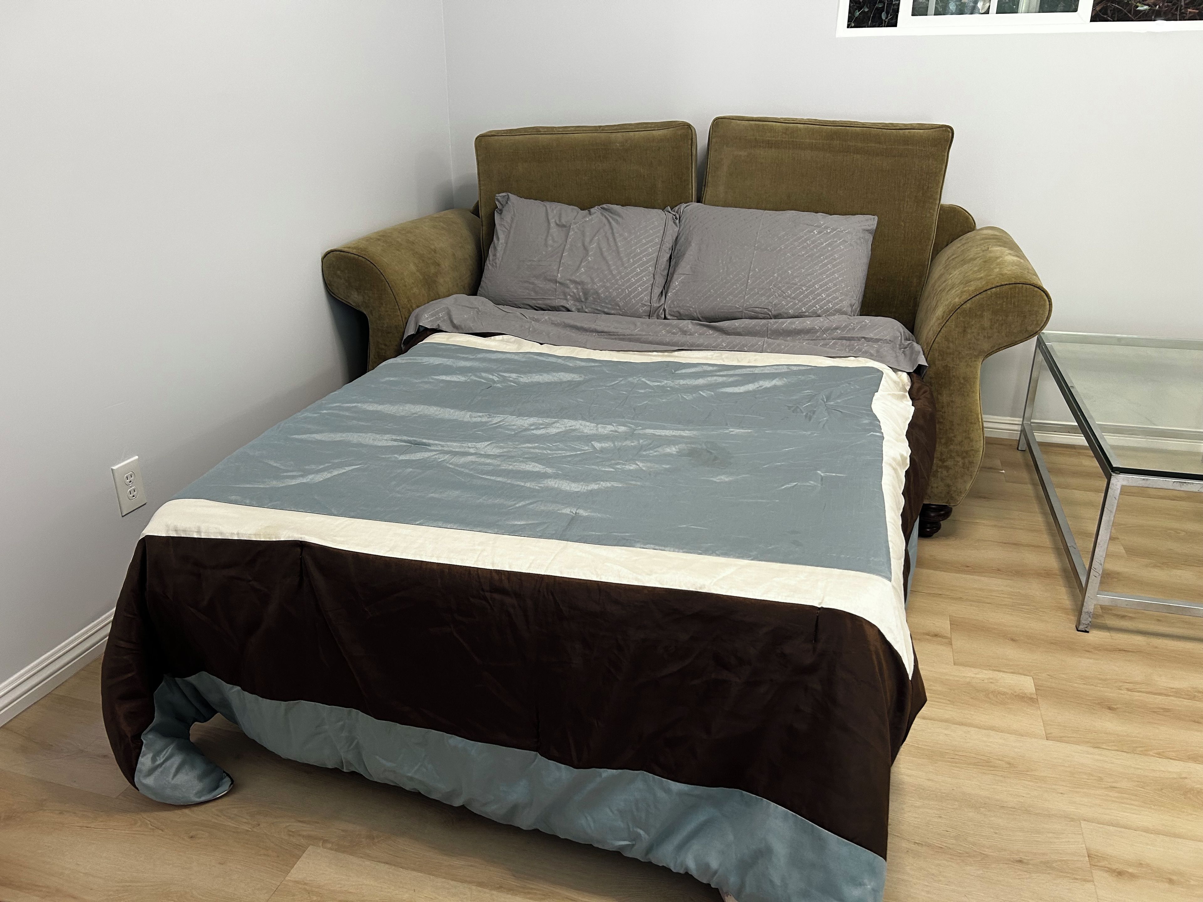 A bed with a grey and white duvet, a brown and blue duvet, and two grey pillows.