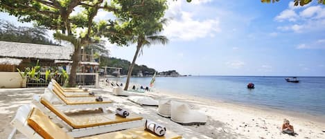 A beachside lounge area with sun loungers, a thatched-roof structure, and a view of the sea.