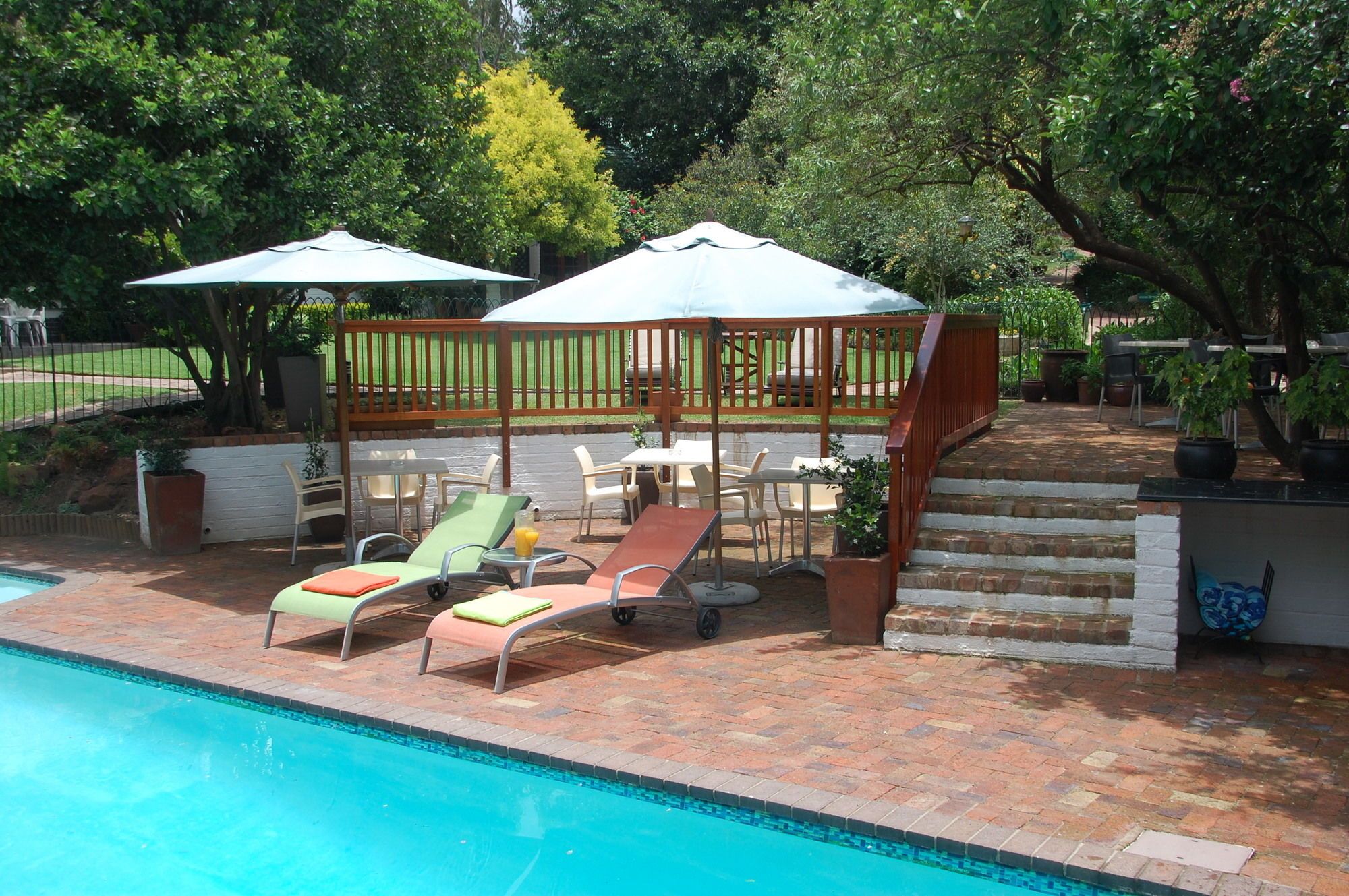 Un espace aménagé au bord de la piscine, avec des chaises longues, un coin salon abrité et un escalier en briques.