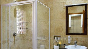 A bathroom with a glass-enclosed shower, a sink with a mirror above it, and beige tiled walls. - Rivonia Bed And Breakfast Garden Estate (Johannesburg)