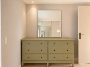 Ein Zimmer mit einem hellen Schminktisch, einer Tür und einem wandmontierten Spiegel.