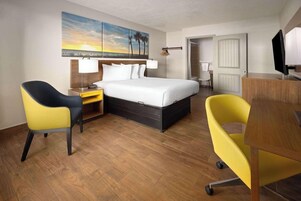 Habitación de hotel con cama, escritorio, dos sillas, televisor y un cuadro en la pared.