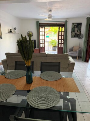 A dining area with a glass table, woven placemats, and a vase with greenery. - Zaboka 3★ – appartement calme et spacieux avec terrasse privative (Petit-Bourg)