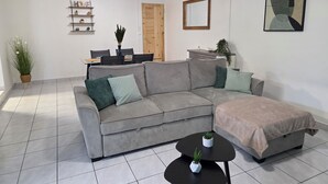 Uma sala de estar moderna com um sofá sectional cinzento, uma pequena mesa de centro preta e um grande quadro abstrato na parede.