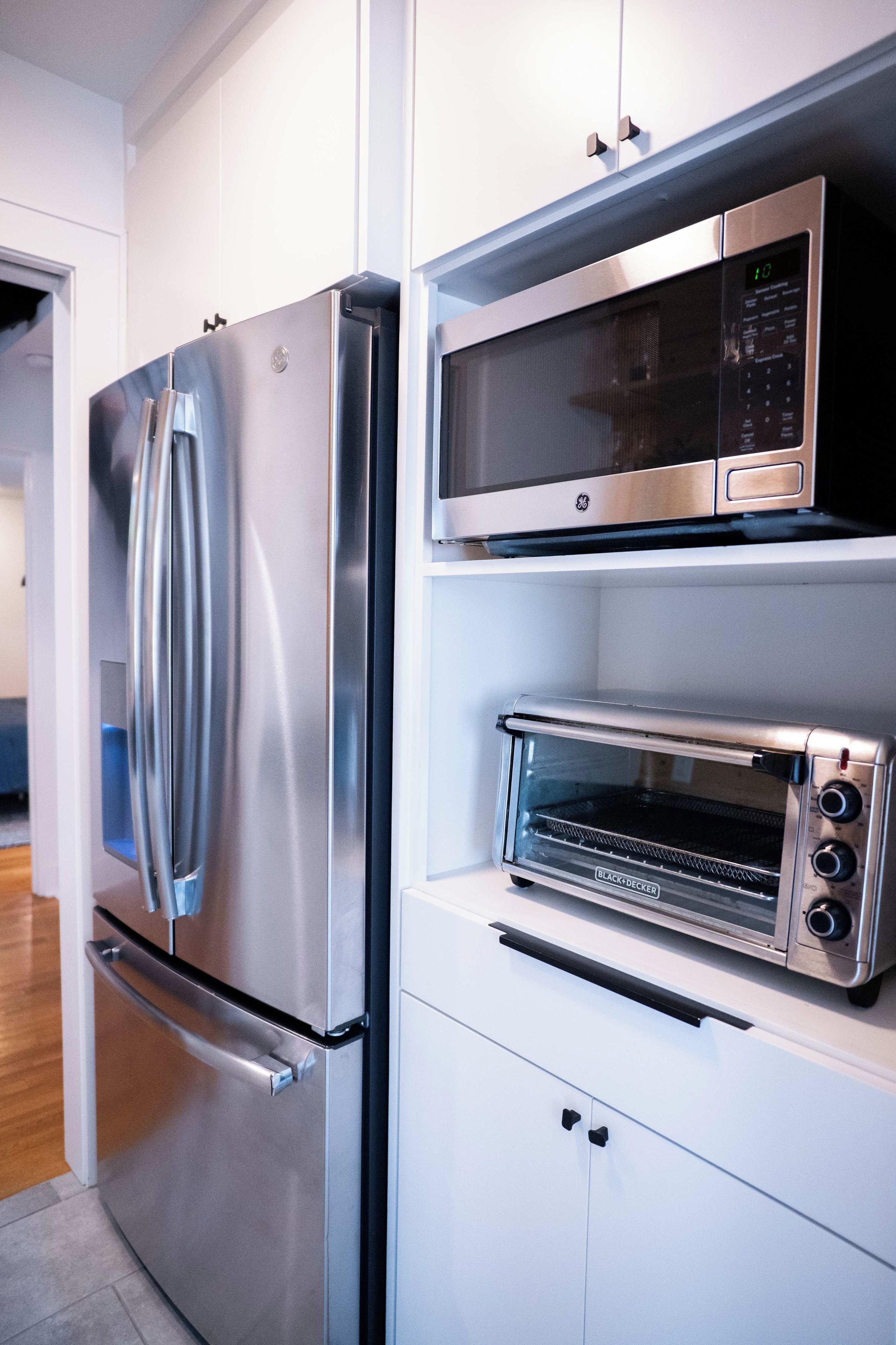A modern kitchen with a stainless steel refrigerator, a microwave, and a built-in toaster oven.