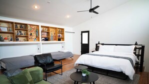 Un dormitorio moderno con cama, dos sofás, una mesita y un ventilador de techo.