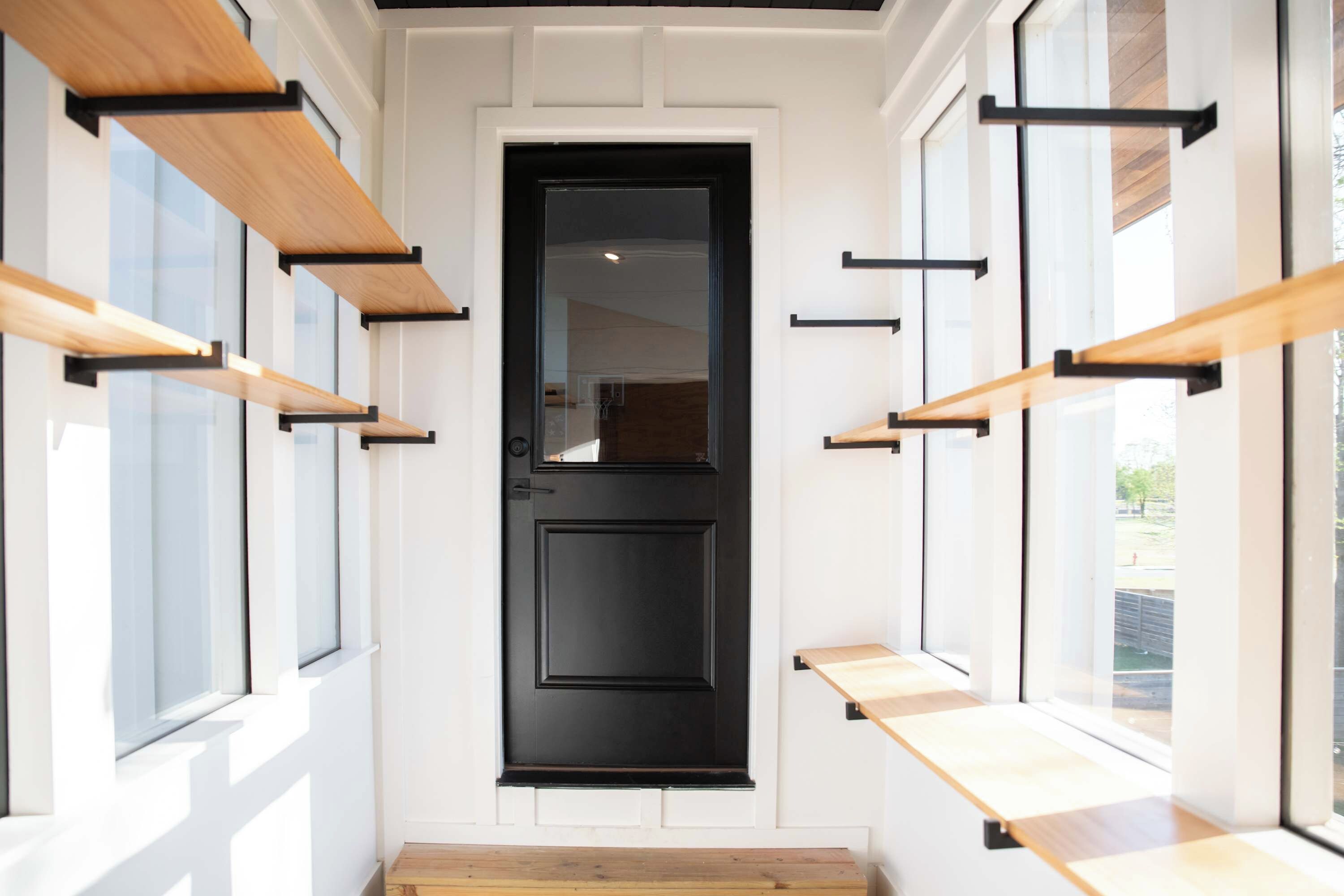 A modern entryway with a black door, wooden shelves, and large windows.