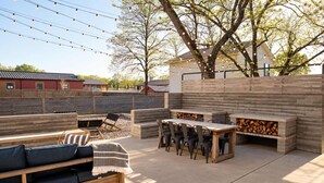 Un patio exterior con un banco de madera, una mesa y sillas, rodeado por una valla de madera y árboles.