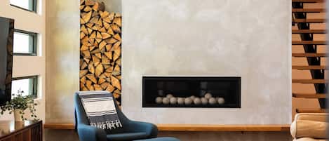 A modern living room with a fireplace, a blue armchair, a coffee table, and a patterned rug.