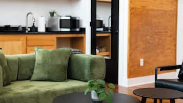 A modern living room with a green sofa, a small round table with a plant, and a black chair.
