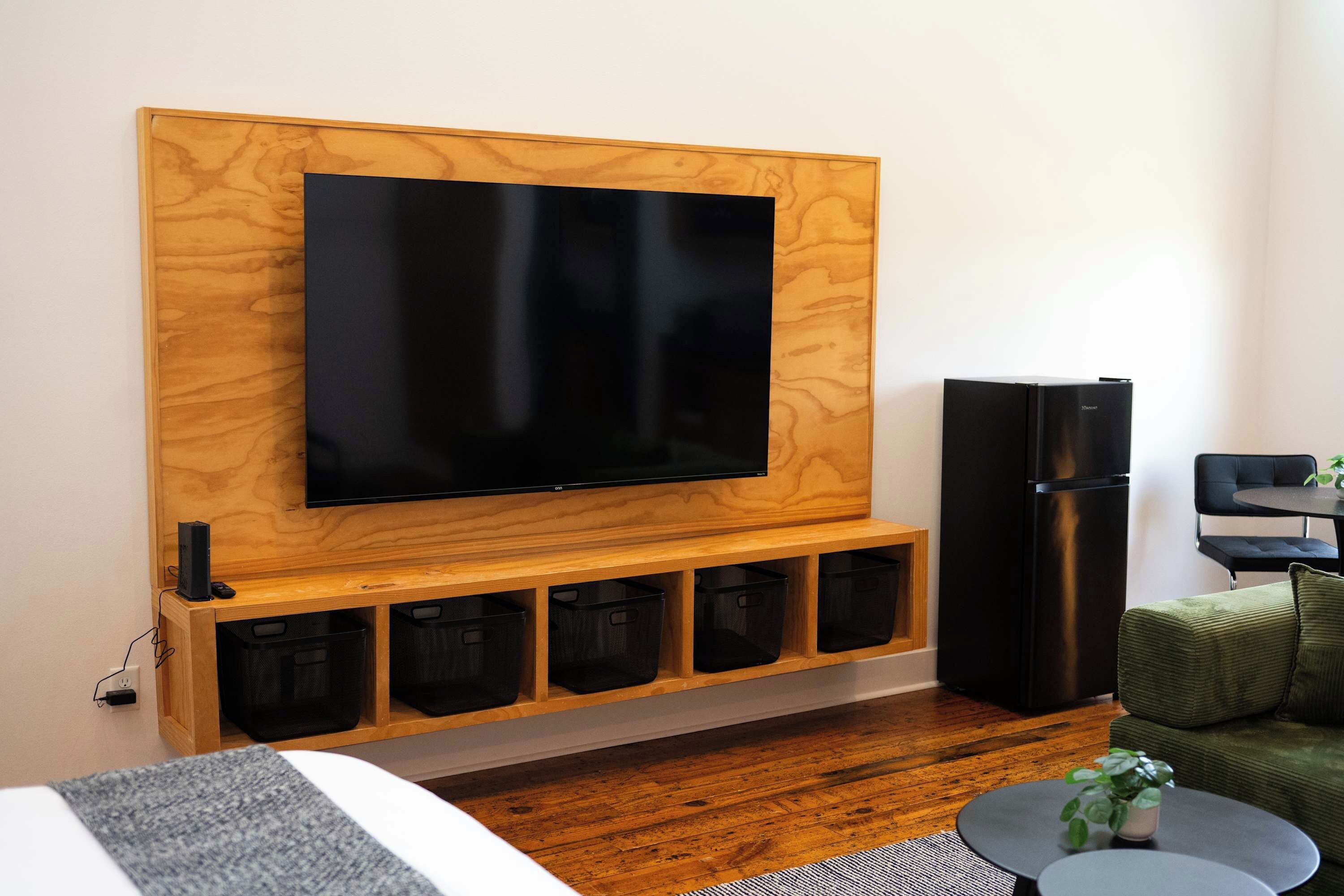 A modern living room with a mounted flat-screen TV, a black refrigerator, and a seating area with a green sofa and a small round table.