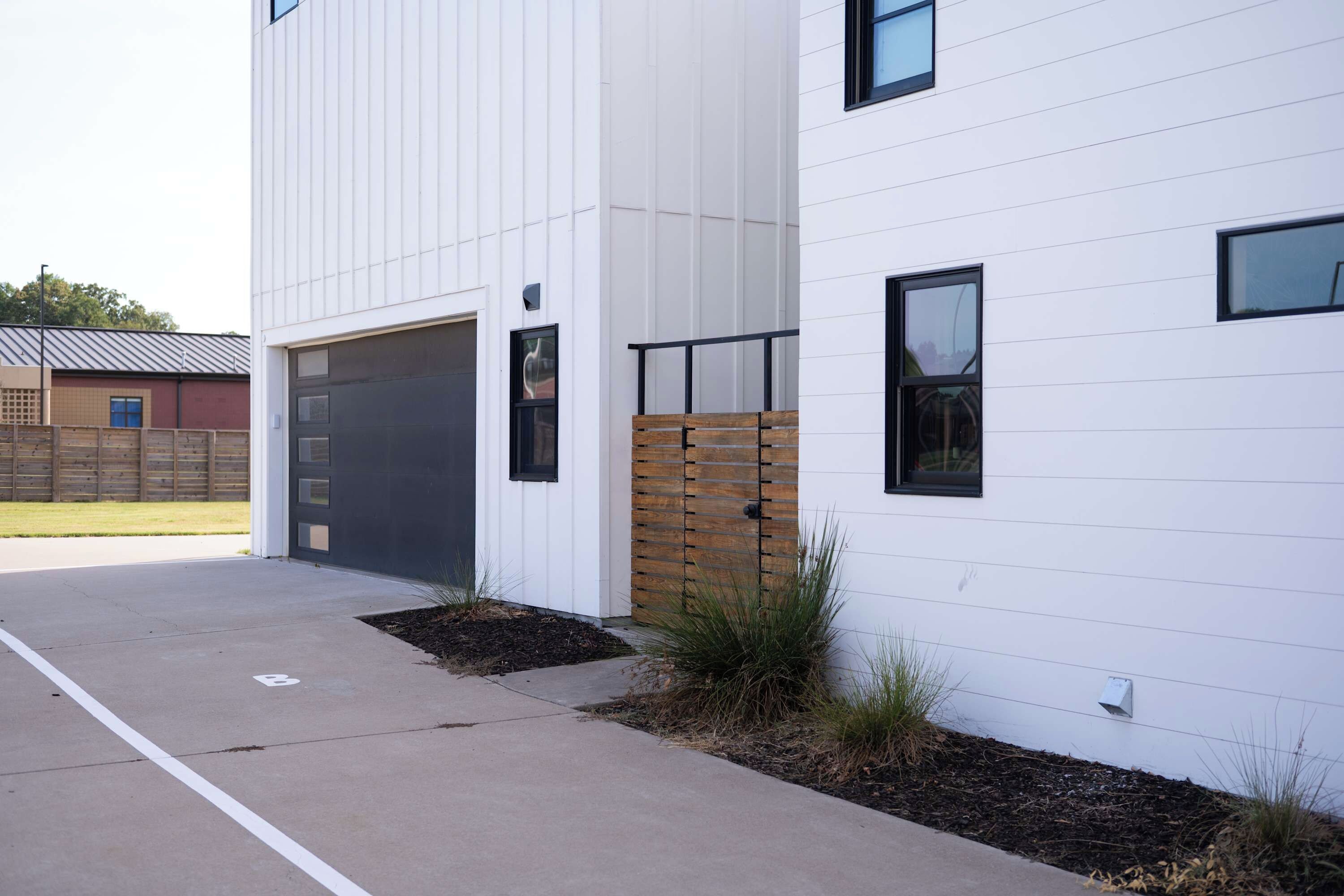 Un bâtiment moderne doté d’une porte de garage, d’une clôture en bois et d’une allée pavée.