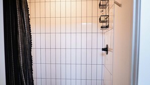 A small bathroom with a white tiled wall, a black shower curtain, a white toilet, and a black floor. - Mid Mod Studio - Garage, Kitchenette, 0.5 mi UCA (Conway)