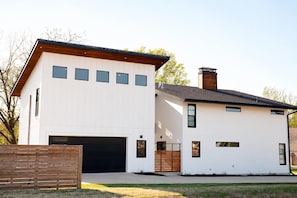 Uma casa moderna de dois andares, com garagem, deck de madeira e chaminé de tijolos.