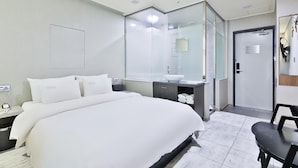 A modern hotel room with a large bed, a bedside table, a bathroom with a sink and mirror, and a door leading to another room. - Oscar Hotel (Busan)