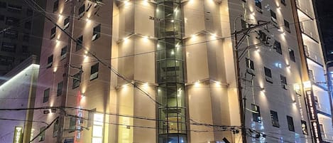 A multi-story hotel with a central glass elevator shaft, multiple balconies, and a well-lit facade.
