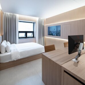 Una habitación de hotel moderna con una cama, un escritorio, un televisor de pantalla plana y un amplio ventanal con cortinas.