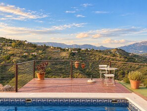 A swimming pool with a tiled edge, a fenced terrace with potted plants, and a table and chair set. - Country House with a Jacuzzi, Pool, and Spectacular Mountain Views (Colmenar)