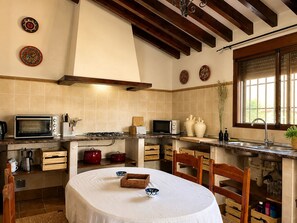 Een keuken met een ronde tafel, houten stoelen, een fornuis, een magnetron en decoratieve borden aan de muur.